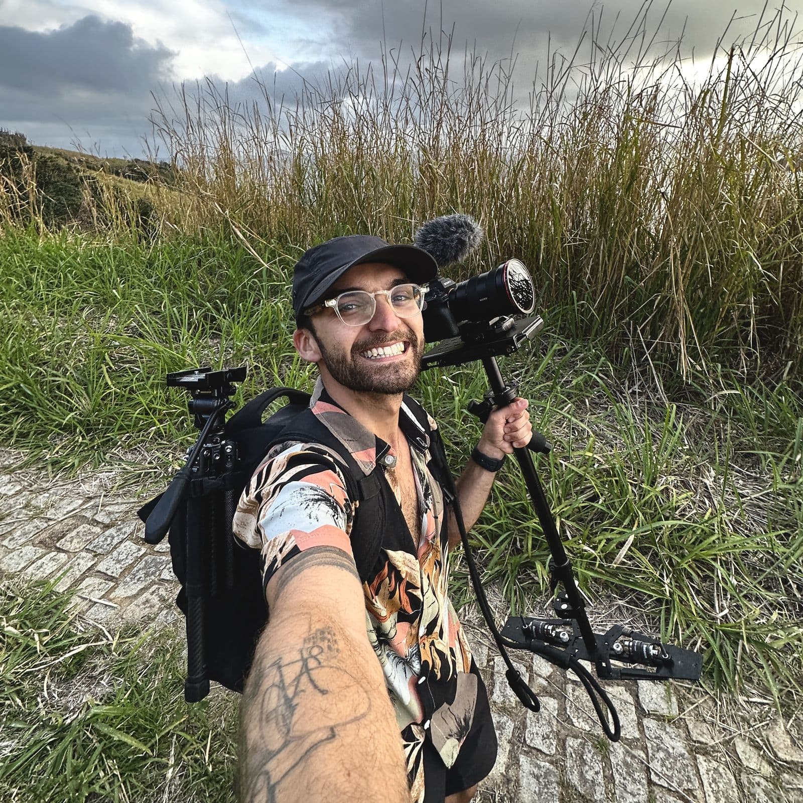 Selfie of Nando with a gear backpack and camera, on a stone path with tall grass