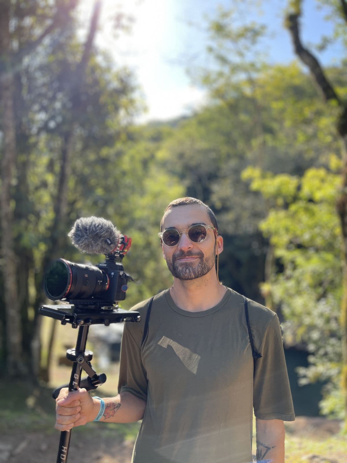 Nando in sunglasses holding a camera on a gimbal, in the middle of the woods