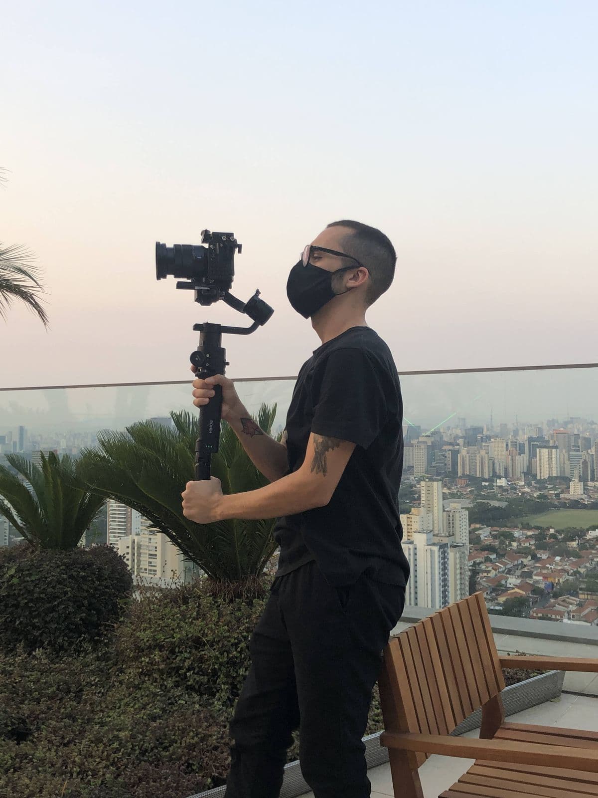 Nando in a mask on a rooftop, with a camera on a gimbal and buildings behind