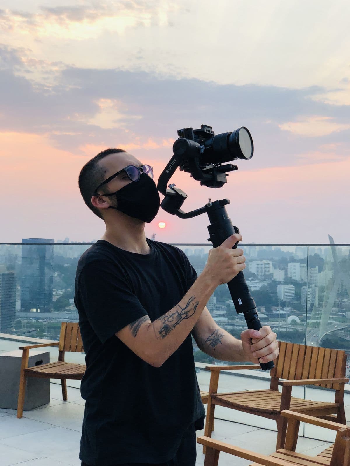 Nando in a mask filming with a gimbal in the late afternoon, the city behind