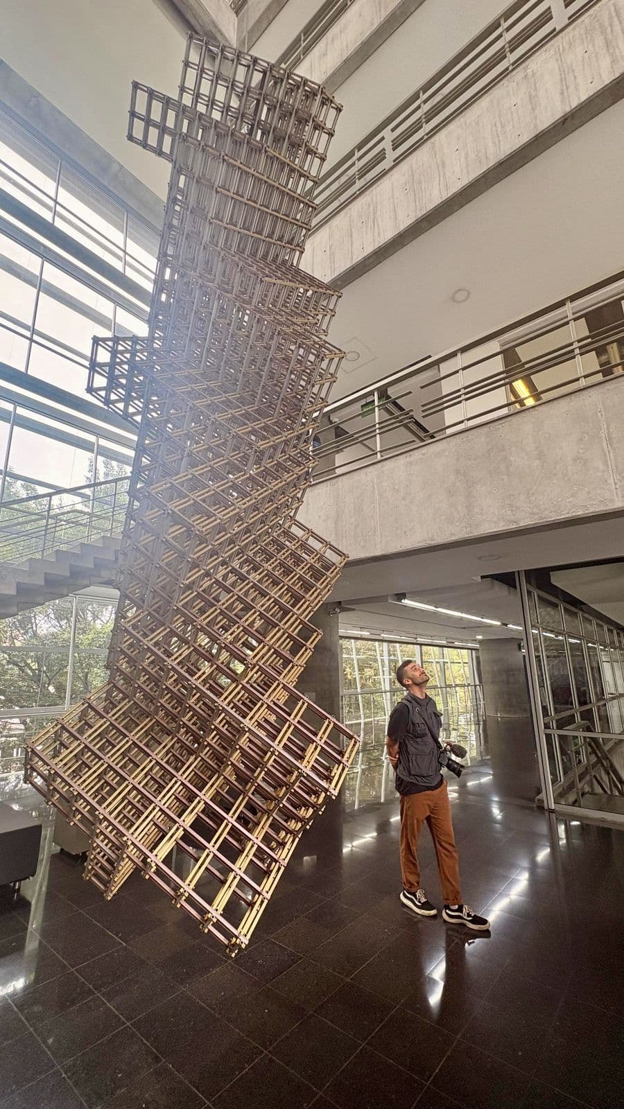 Nando looking up, next to a tall wooden sculpture in a lobby