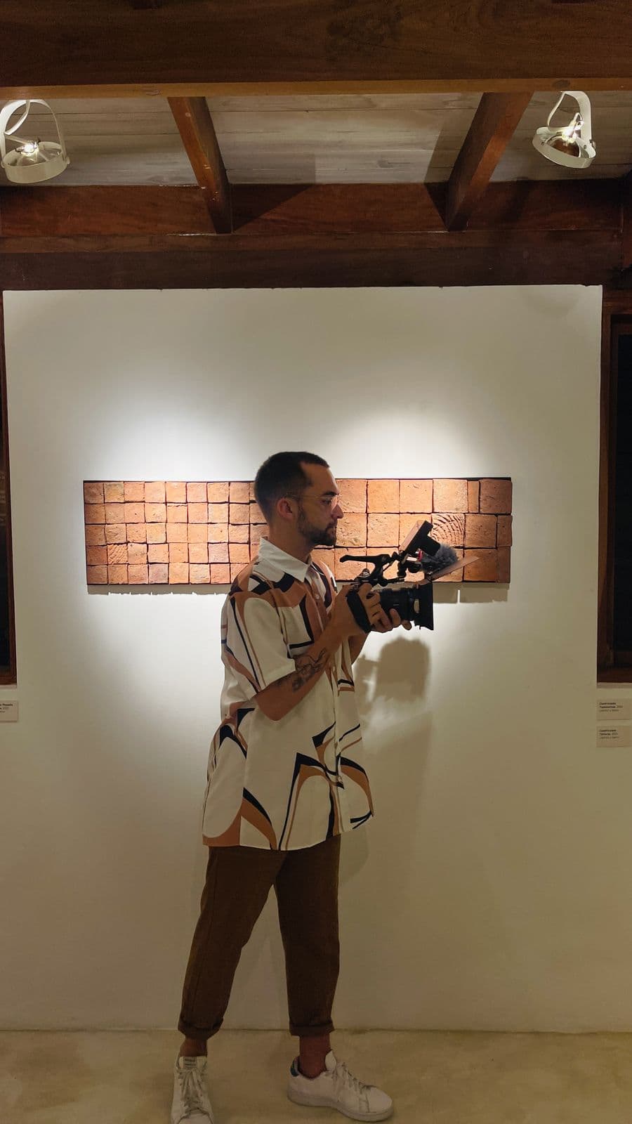 Nando filming in front of a brick piece hanging on a white wall