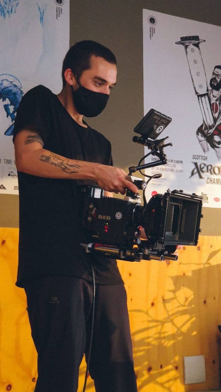 Nando in a mask, holding a cinema camera with a monitor