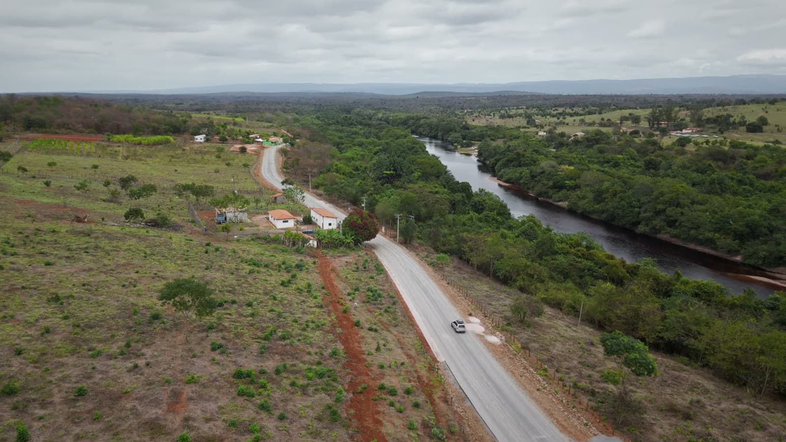 Vista aérea de uma estrada de asfalto ao lado de um rio cercado de mata, com um carro passando e o cerrado ao redor