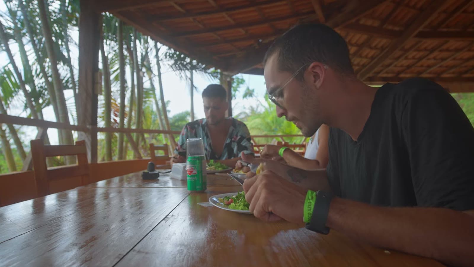 Nando almoçando na varanda de madeira do restaurante do parque, com um prato de comida na mesa