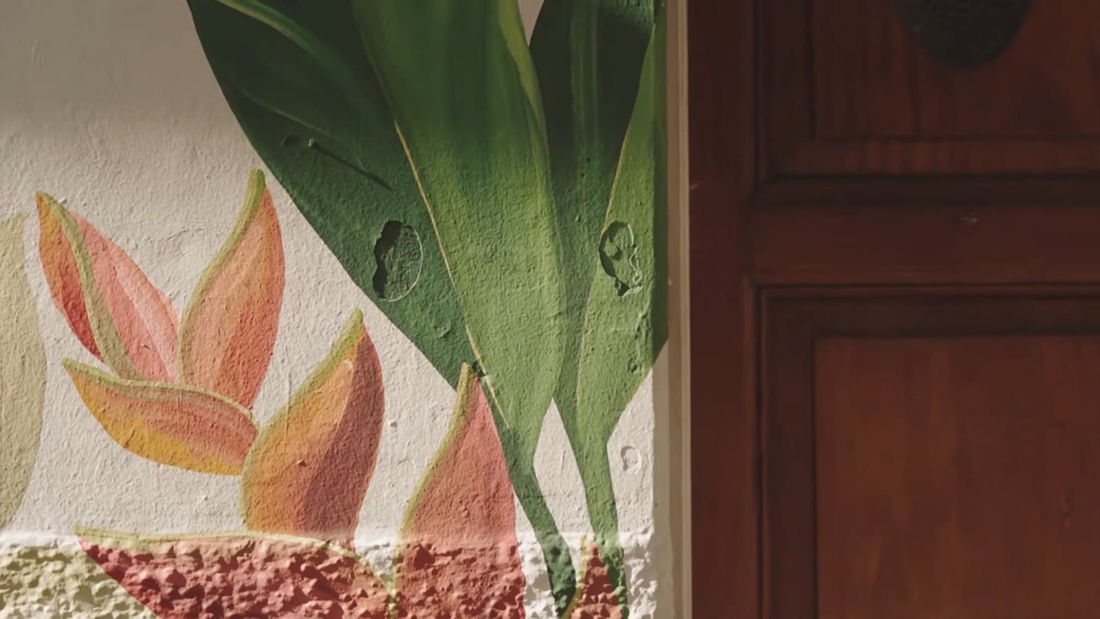 Hojas pintadas en un muro, junto a una puerta de madera
