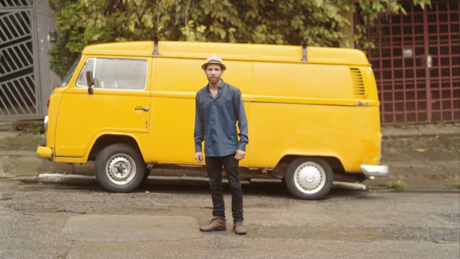 Un hombre de sombrero frente a una Kombi amarilla
