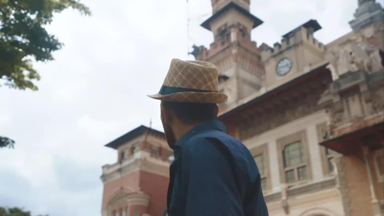 Un hombre de sombrero frente a un palacio antiguo con torres y reloj