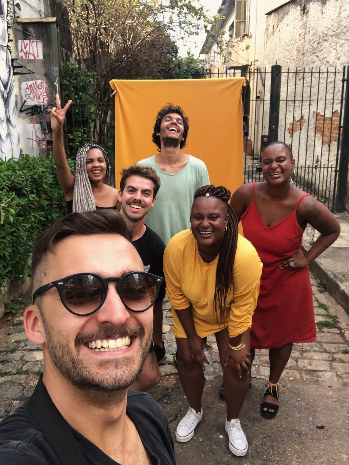 Selfie del equipo con Nayara y Yara, frente al fondo amarillo montado en un callejón