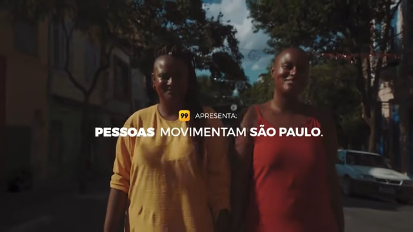 Dos mujeres caminan por una calle arbolada; sobre ellas, el título “99 presenta: las personas mueven São Paulo”