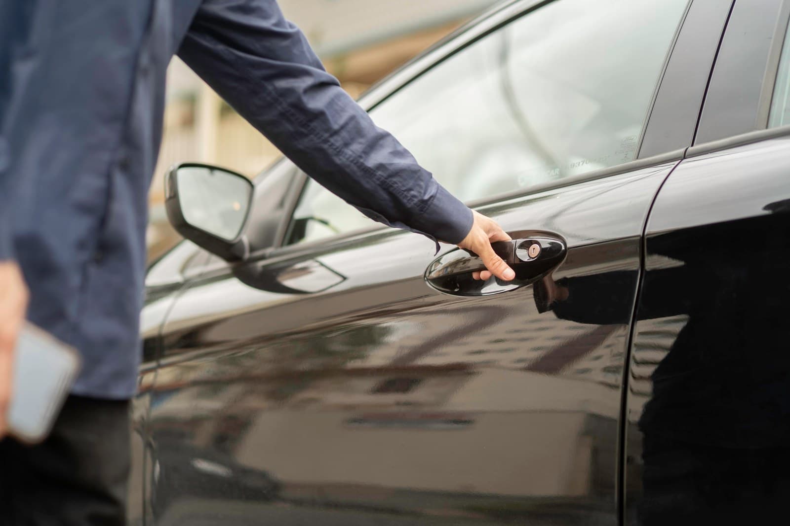 Una mano con guante abre la puerta de un auto negro