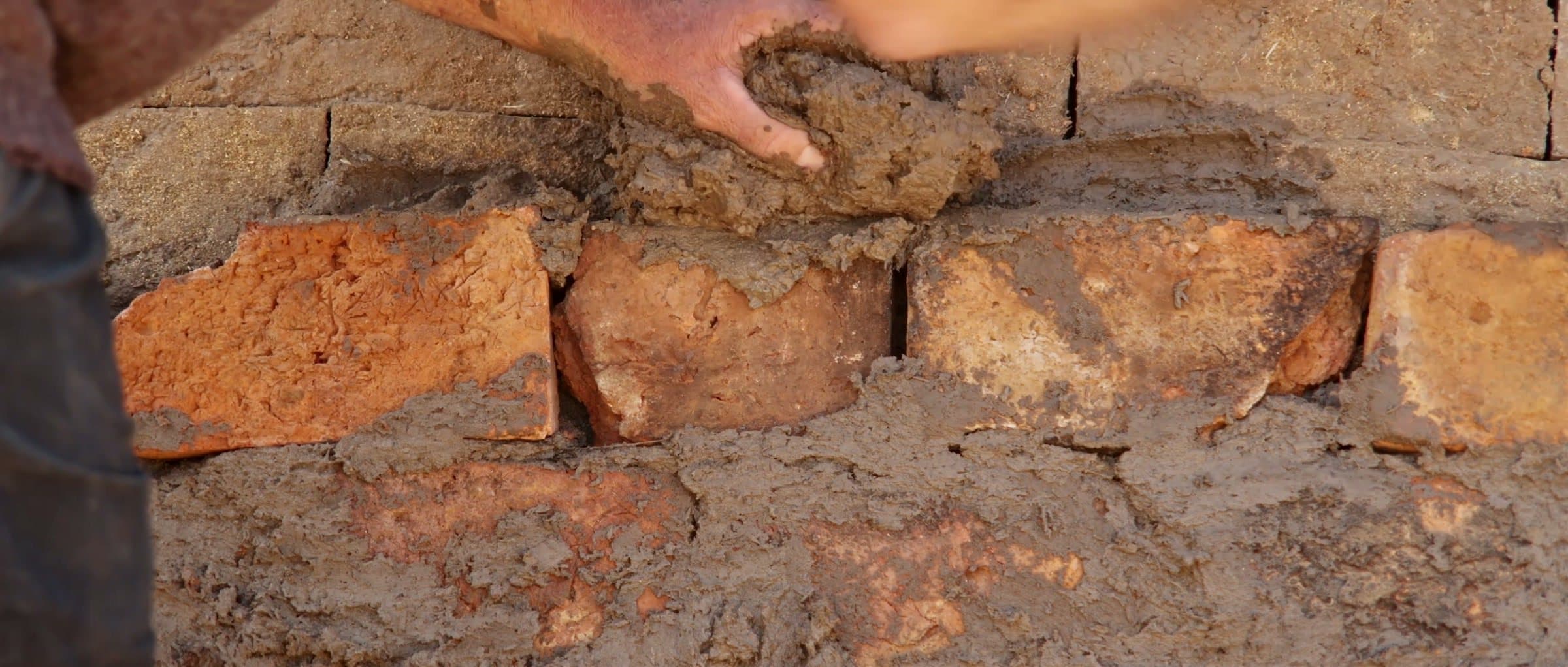 Hands holding clay over the bricks