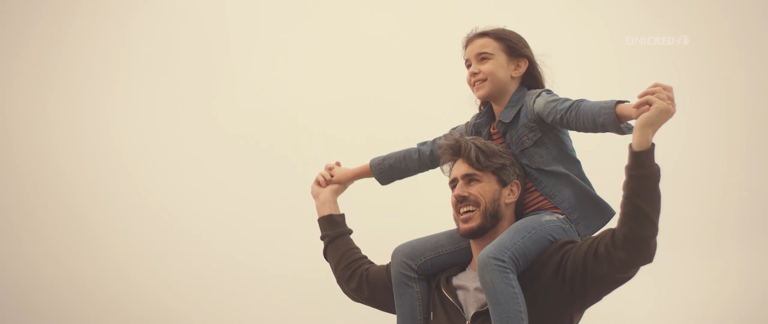 A man carries his daughter on his shoulders, both with arms open