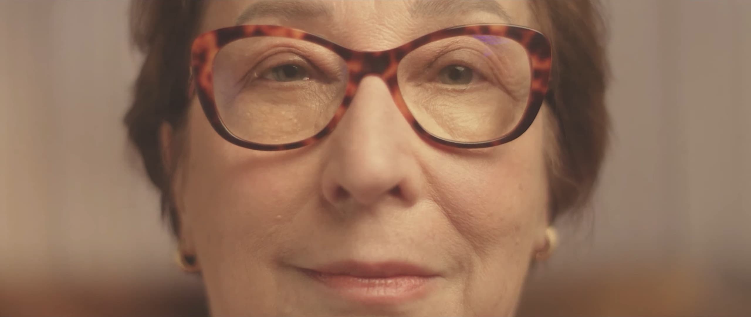 An older woman in red glasses smiles at the camera