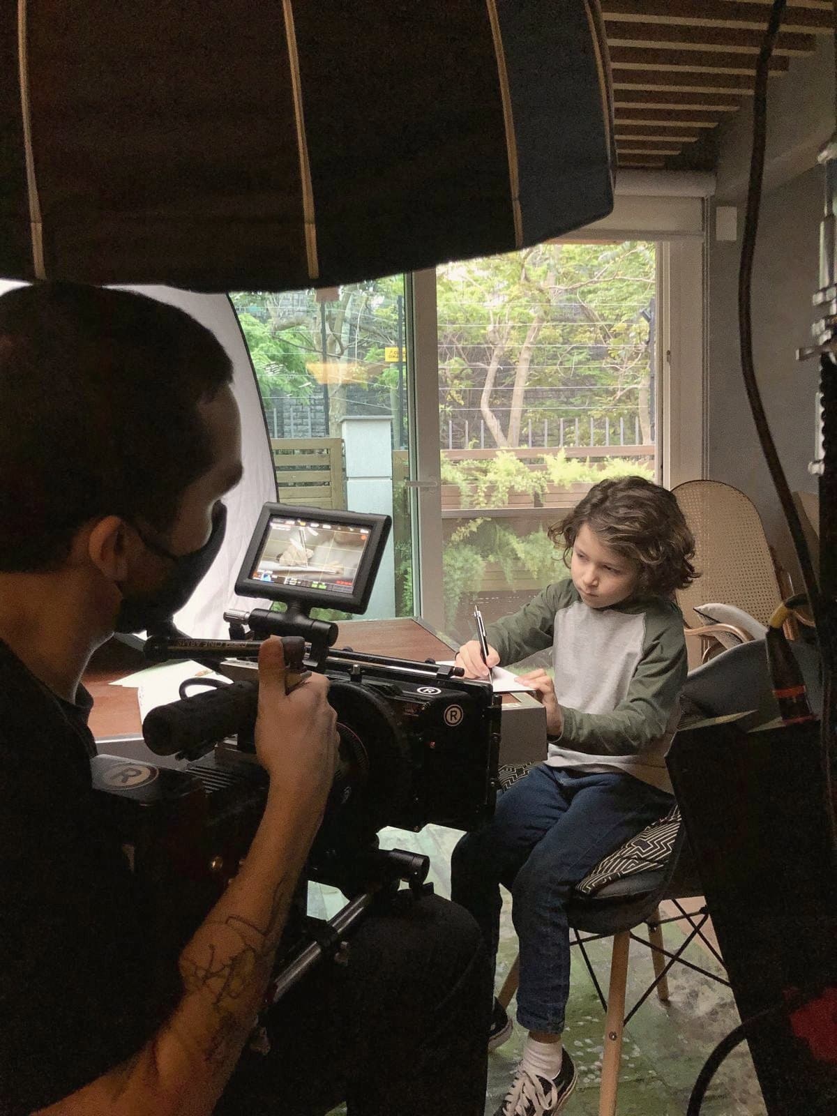 Nando films a child drawing, with the set lights overhead