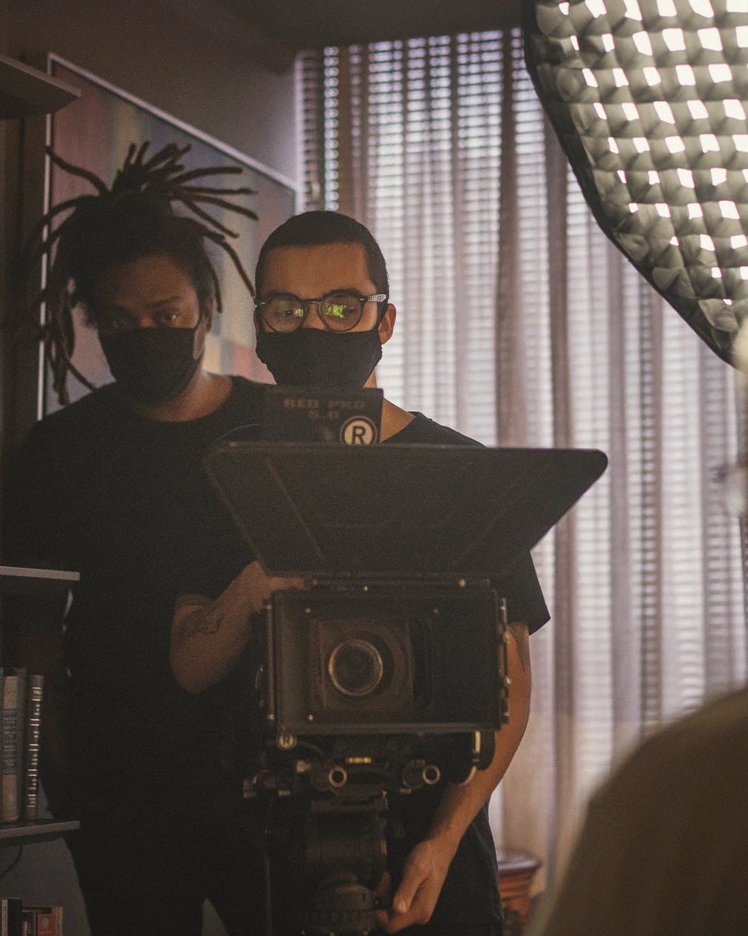 Two masked technicians behind the camera, a softbox beside them