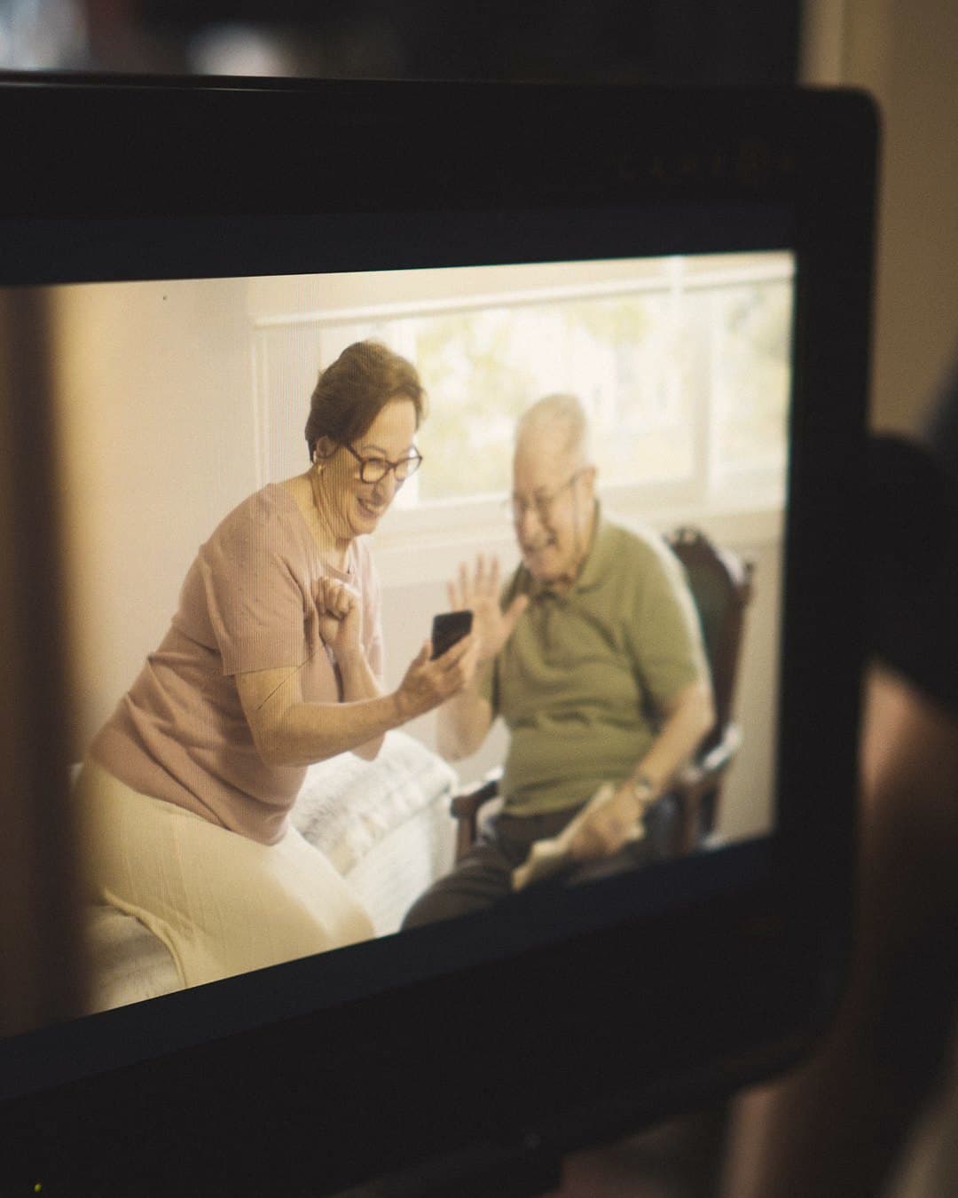 The camera monitor shows the older couple with the phone