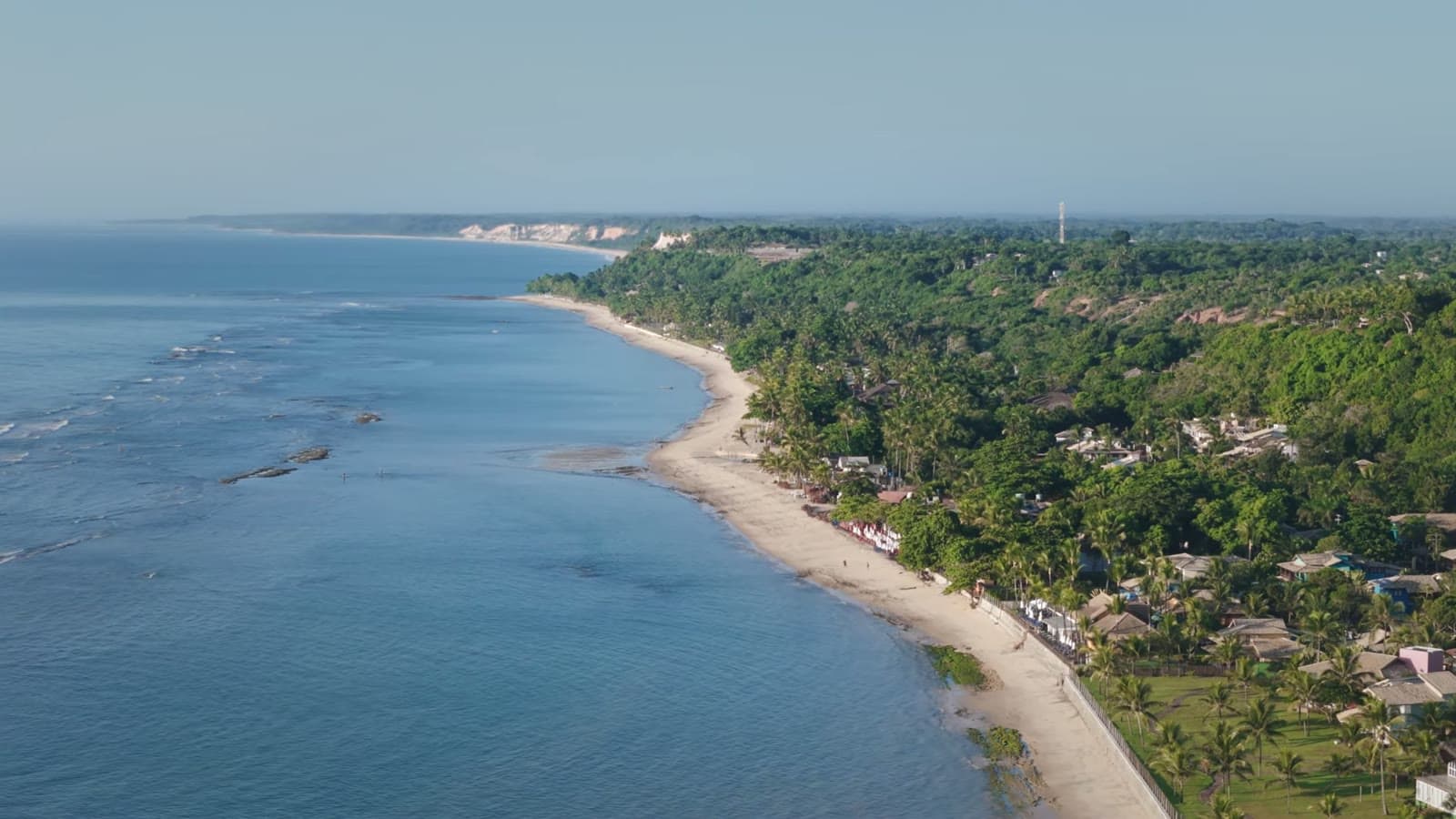 Aerial view of the Mucugê shoreline, with the strip of sand, the palm trees and the houses between the forest and the blue sea
