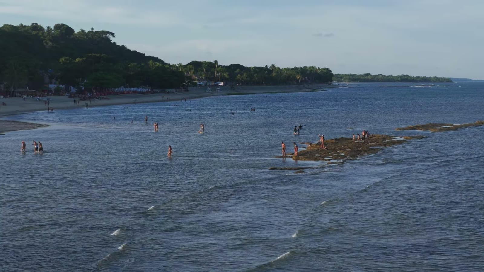 People walking in the shallow sea, near a strip of reef that shows up at low tide