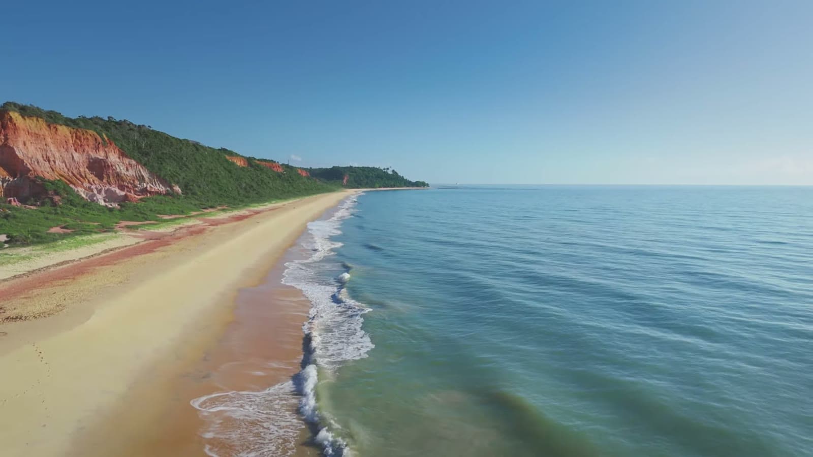Aerial view of a long beach at the foot of the cliffs, with the calm, greenish sea