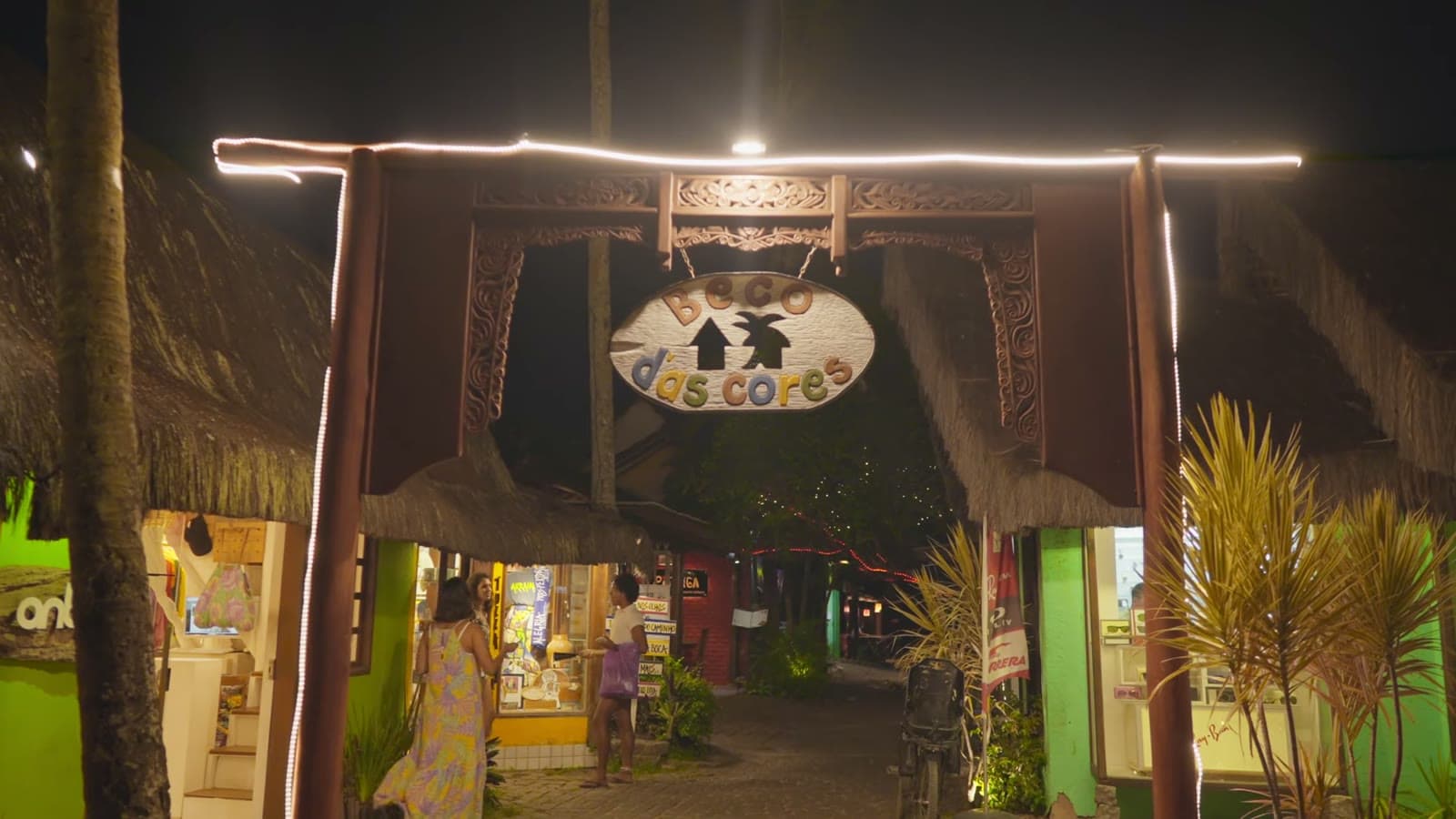 Lit wooden gateway with the Beco das Cores sign, at night, with colorful little shops on both sides