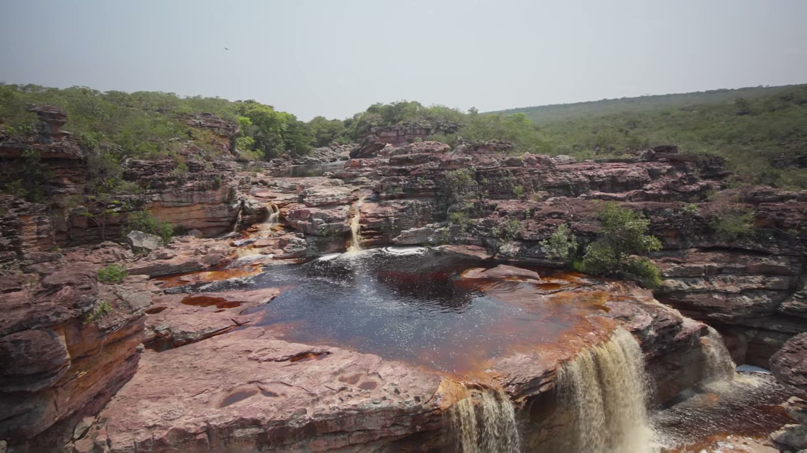 Aerial view of a dark-water pool among the rocks, with small waterfalls flowing out of it