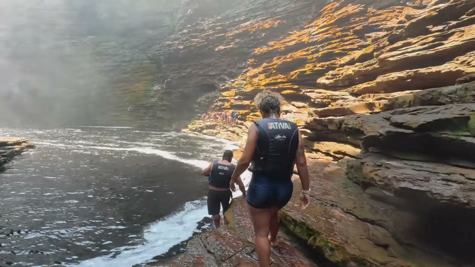 Two people in life jackets walking over the rocks at the edge of the canyon's dark water