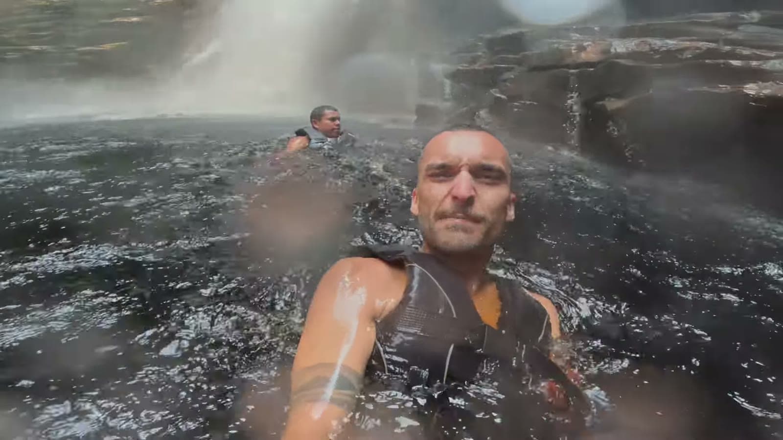 Nando in the water, wearing a life jacket, near the falls of Cachoeira do Buracão