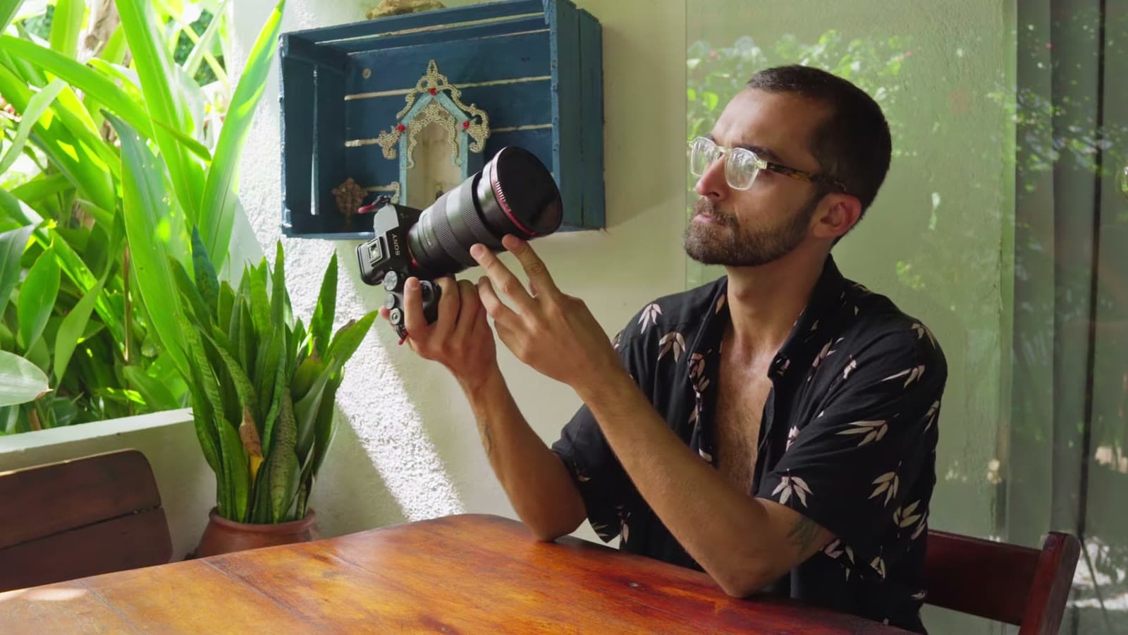 Nando sentado à mesa, segurando a câmera com uma lente de cinema manual