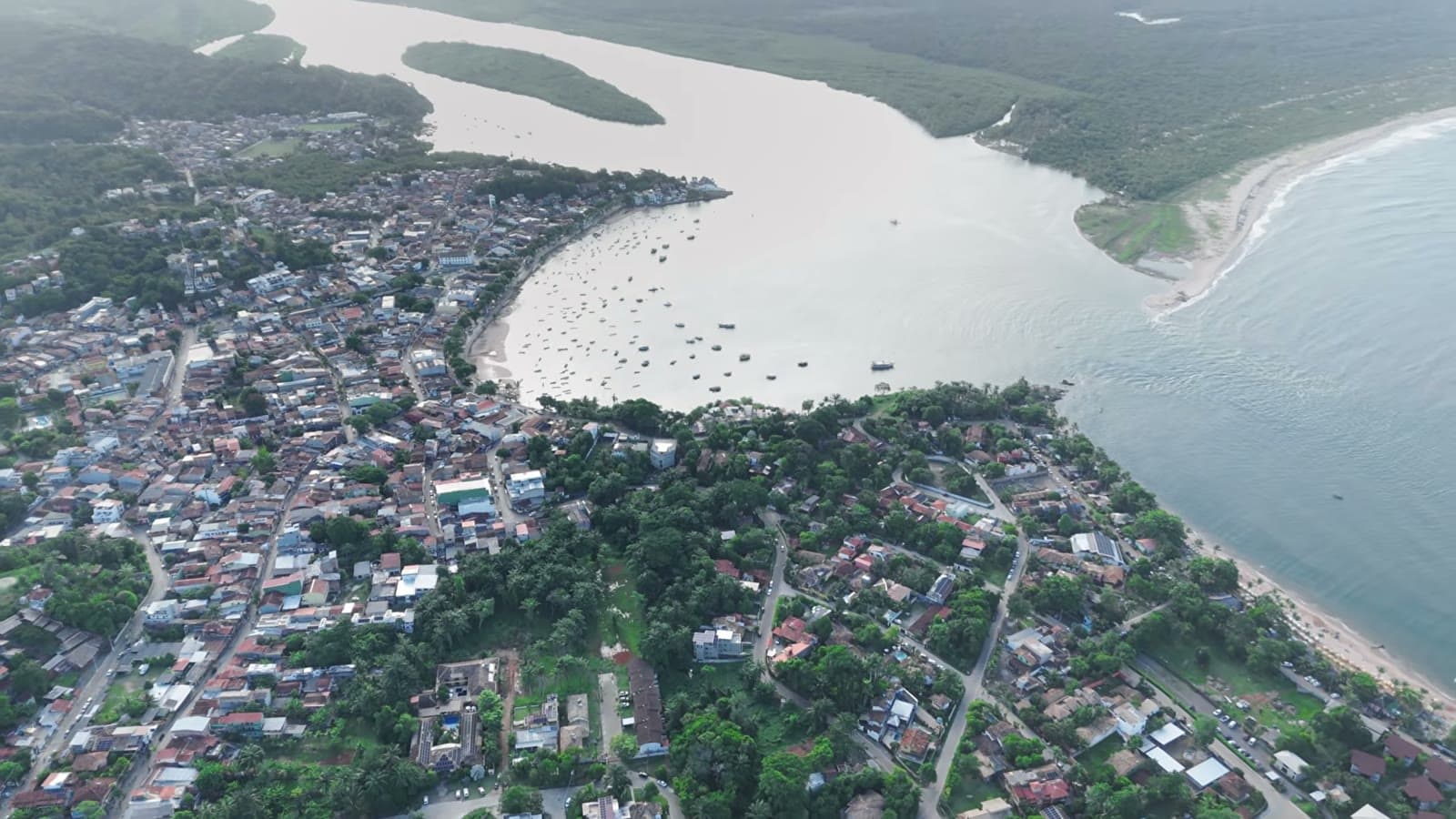 Aerial view of Itacaré, with the town's houses, the wide river full of boats and the sea in the background