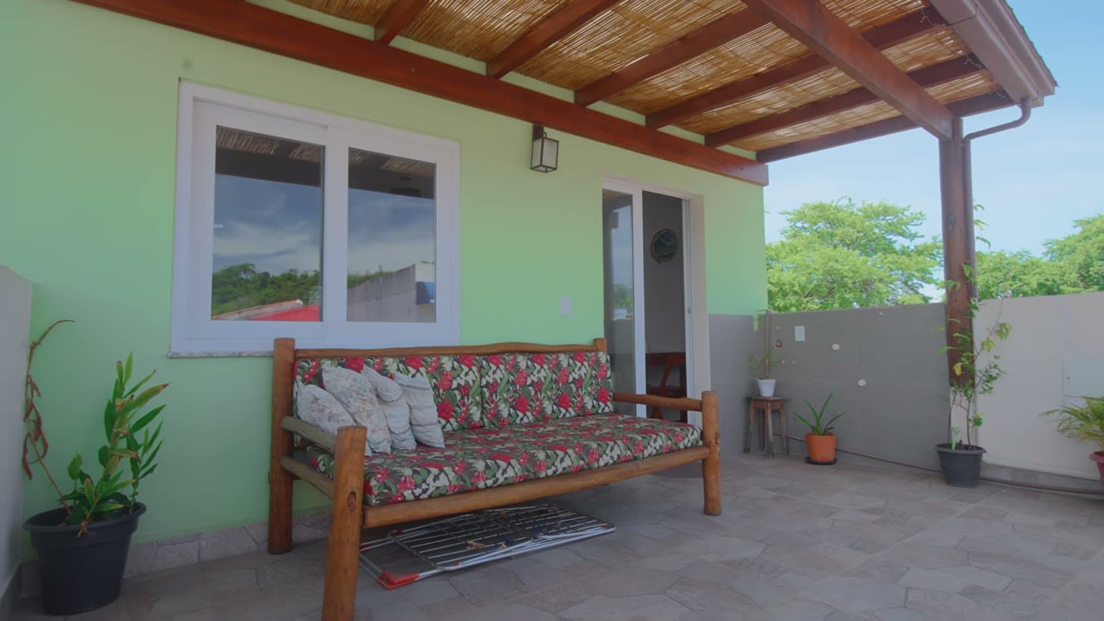 The penthouse terrace, with a wooden sofa with floral cushions, plants and the light green wall