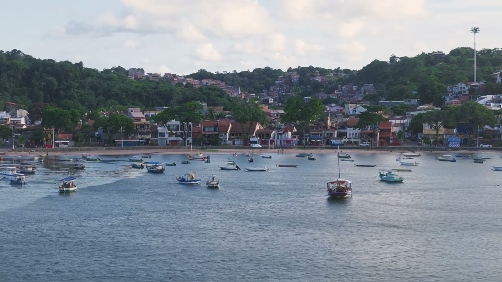 Fishing boats anchored on the calm water of Praia da Coroa, with Itacaré's houses in the background