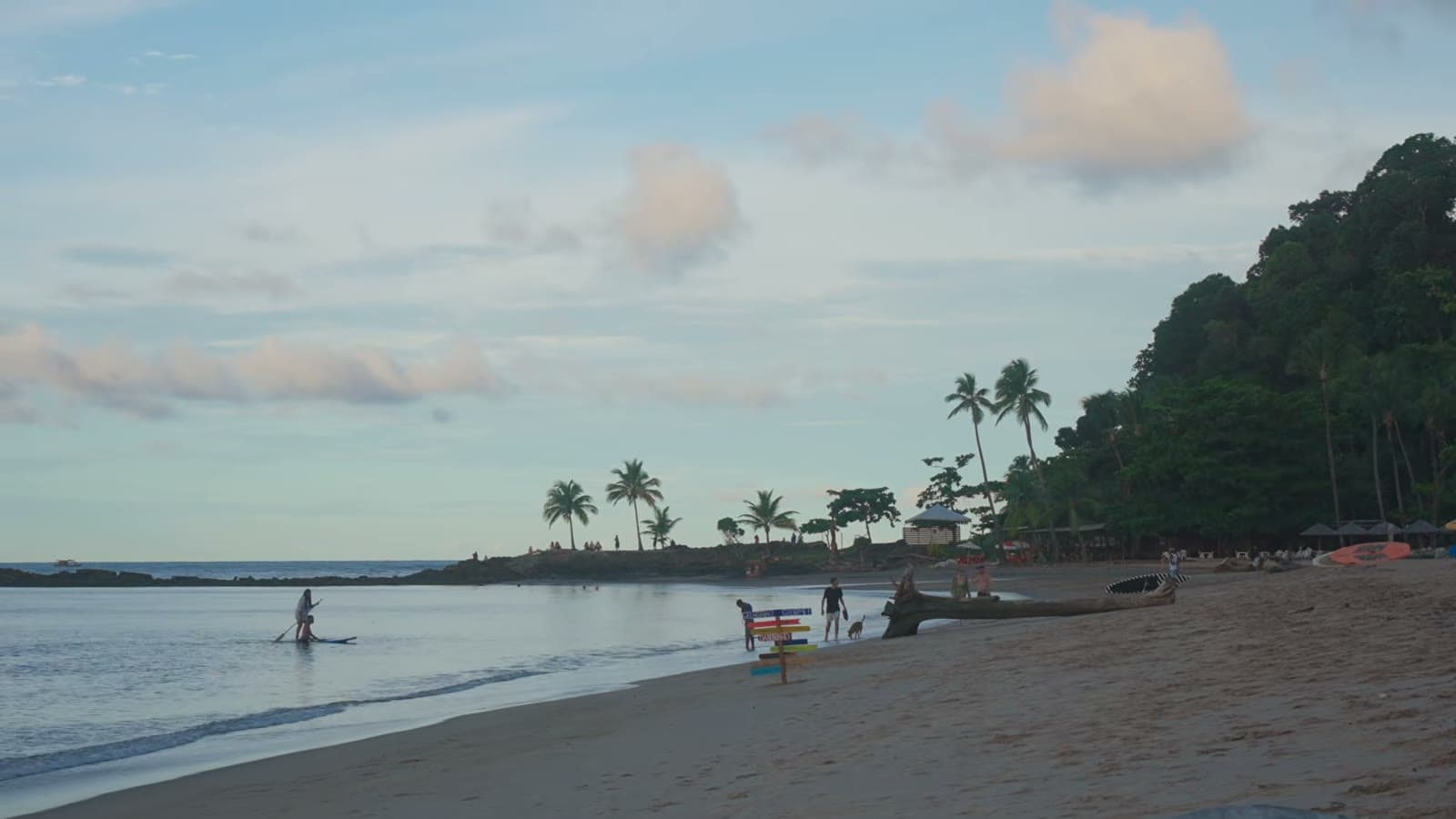 Praia da Concha in the late afternoon, with people in the calm sea and palm trees on the point in the background
