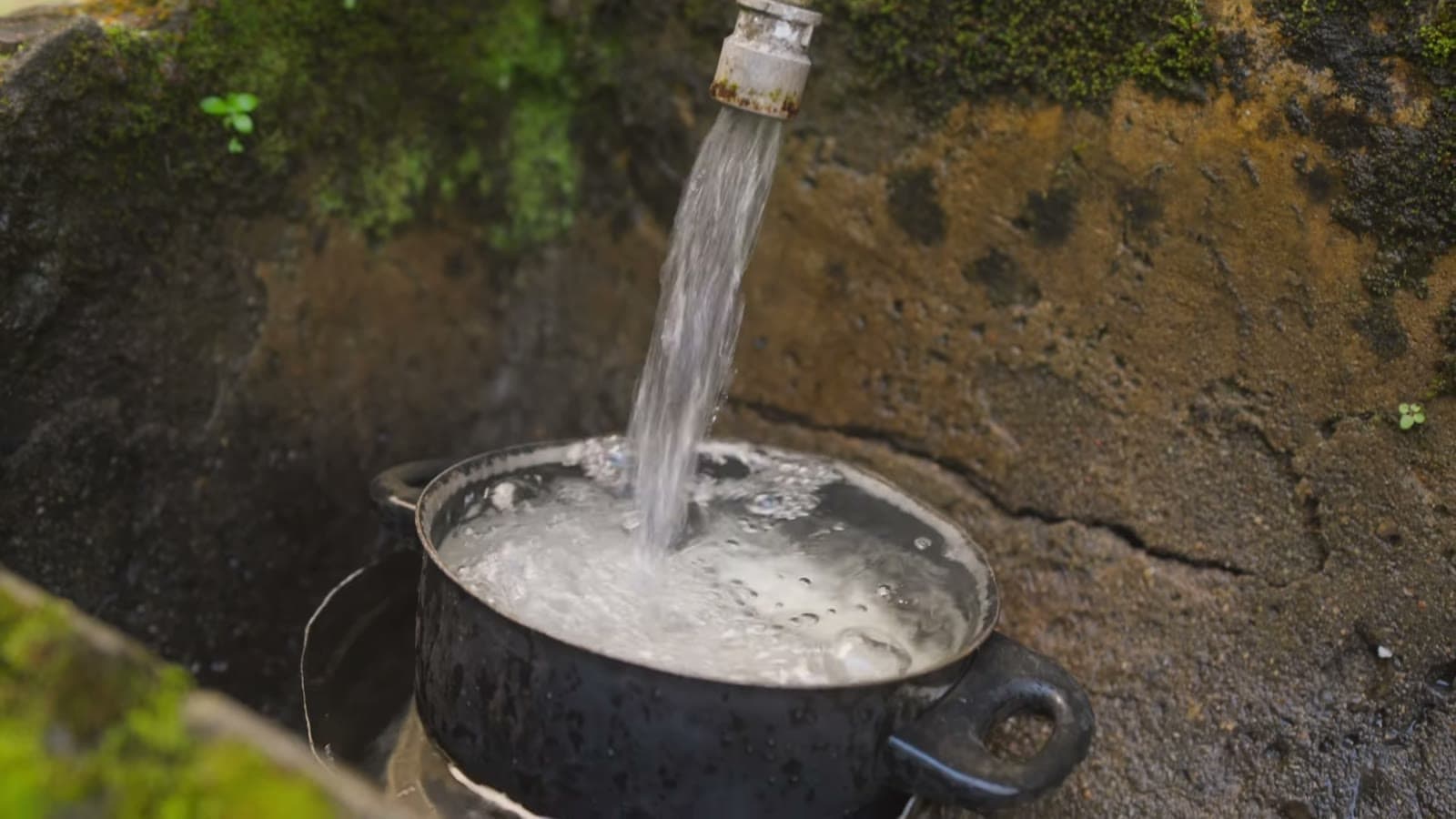 Crystal-clear water pouring from a tap fixed to the rock into a pot