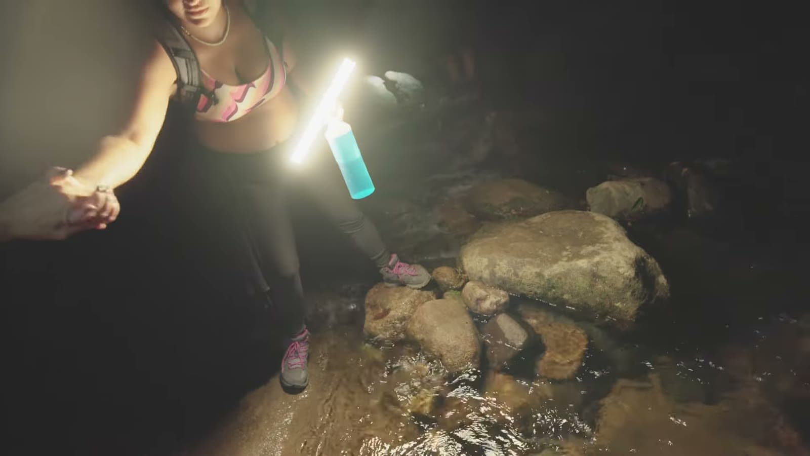 Camila reaches out a hand in the dark, holding a flashlight, to help with a stream crossing among rocks