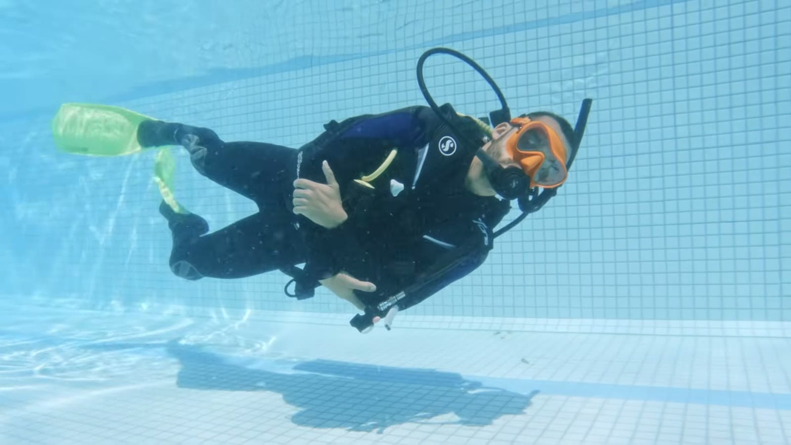 Diver in an orange mask and green fins floating at the bottom of a blue pool