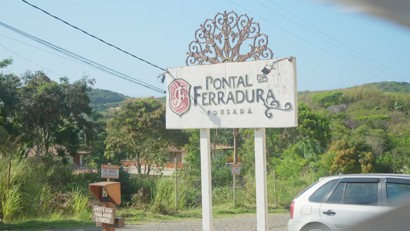 Sign for Pousada Pontal Ferradura by the roadside, with forest and hills in the background