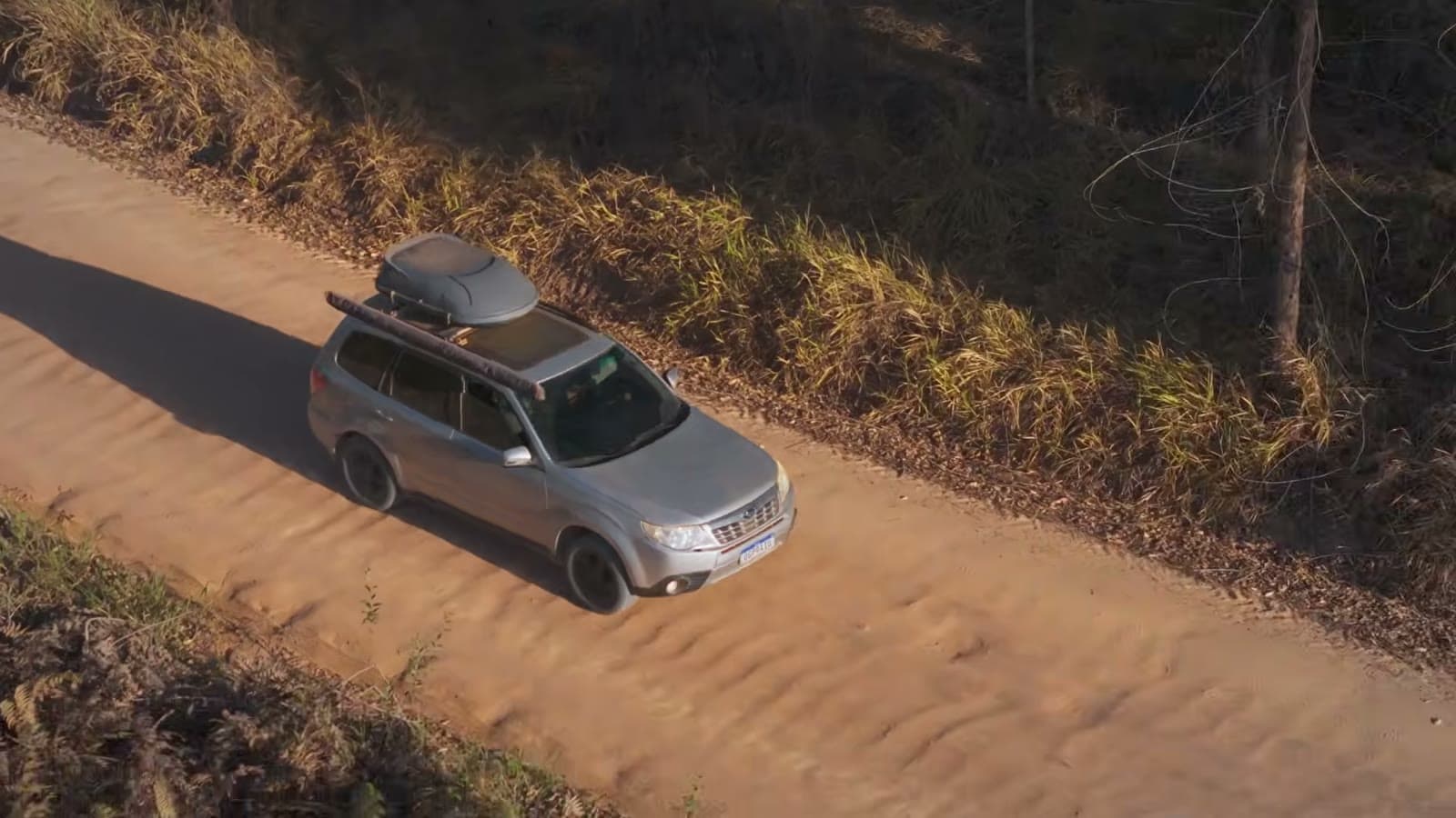Vista aérea do Subaru Forester prata, com bagageiro no teto, numa estrada de areia entre a vegetação