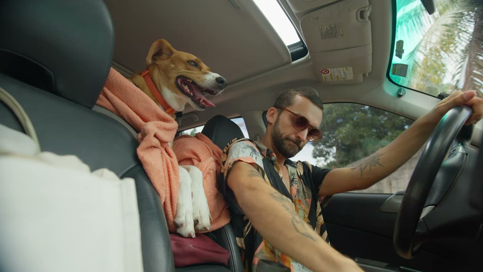 Nina sitting in the car seat, tongue out, next to Nando driving in sunglasses