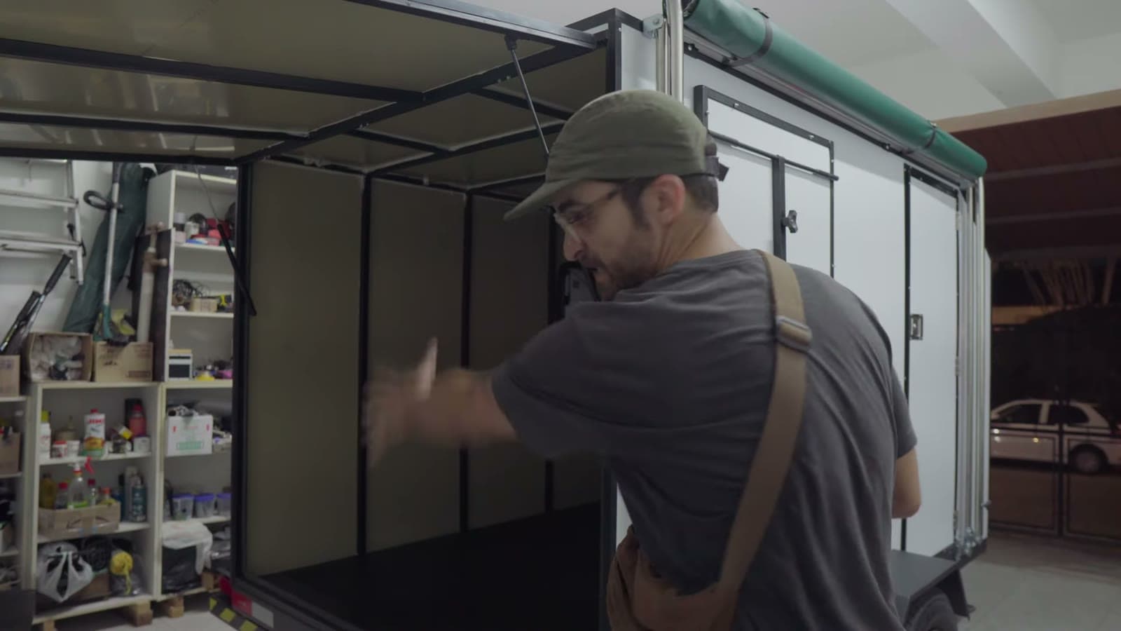 Frame of a mini trailer in a workshop, with a person in a cap putting up the walls