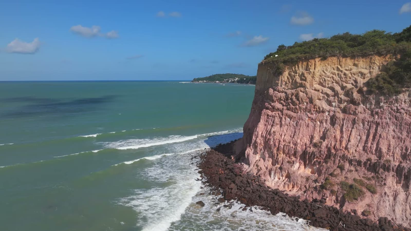 Reddish earth cliff over the blue-green sea, seen from the drone