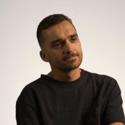 Nando Martins, seated portrait in a black t-shirt against a light studio background