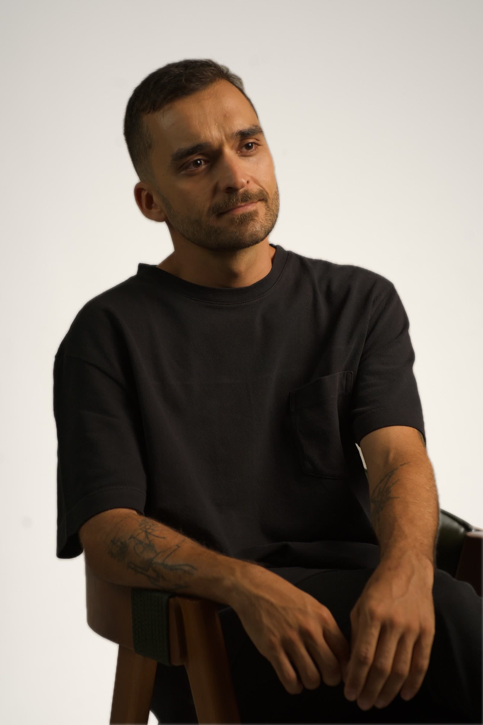 Nando Martins, seated portrait in a black t-shirt against a light studio background