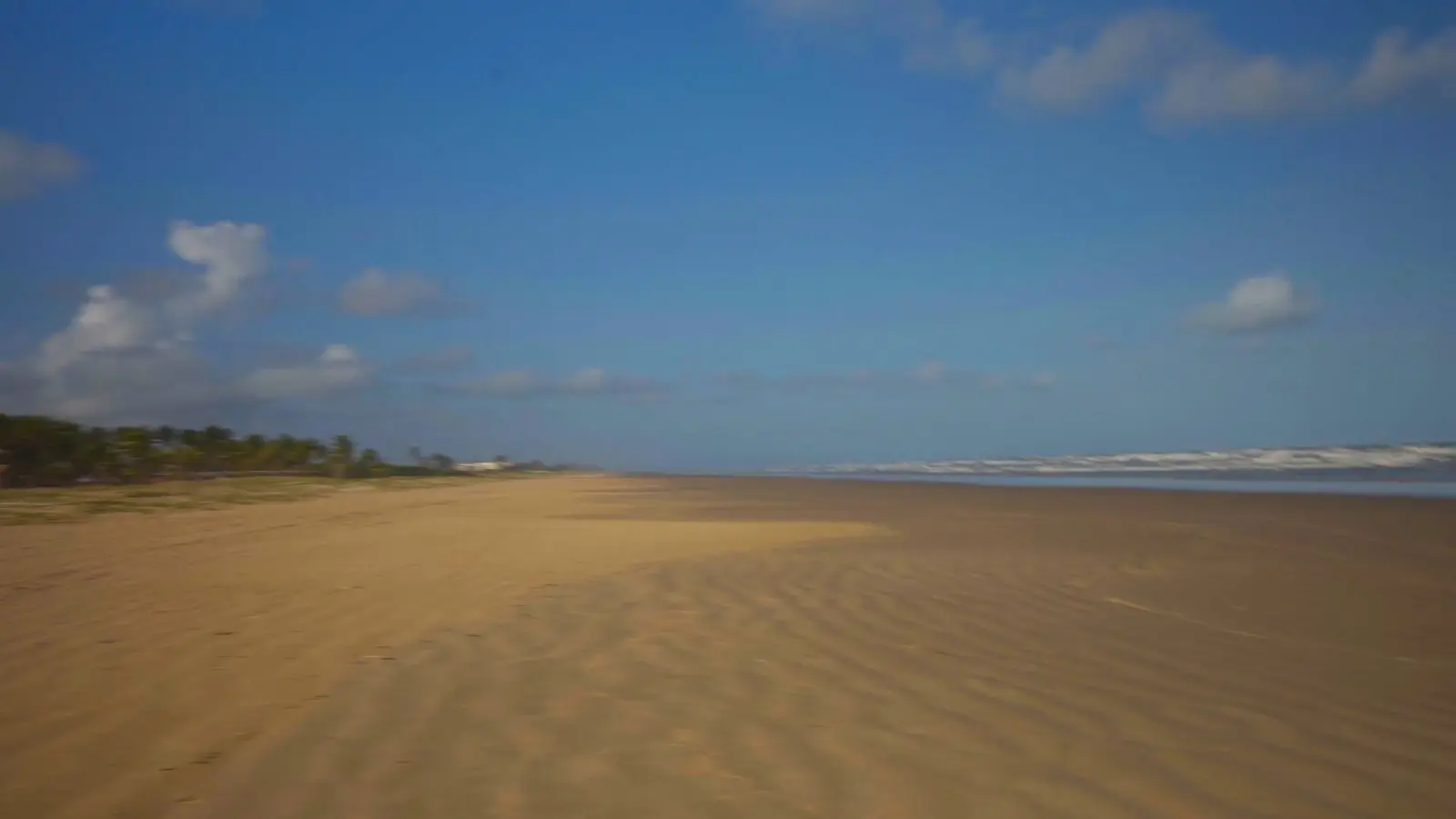 A praia de Aracaju na maré baixa, com uma faixa larga de areia e o céu azul