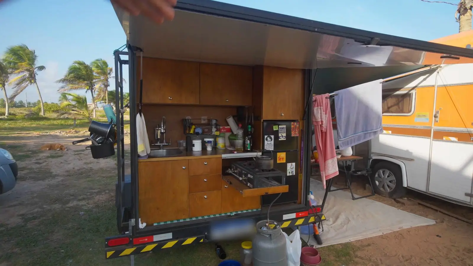 A cozinha do mini trailer aberta para fora, com armários de madeira, pia, fogão e geladeira