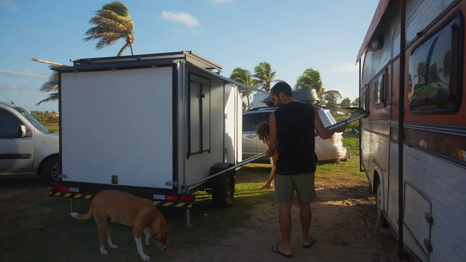Nando recolhendo o toldo do mini trailer enquanto a Nina fareja o chão