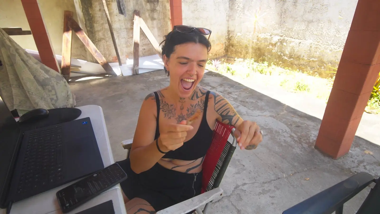 A Lelê sentada à mesa de trabalho, rindo com a cara de quem acabou de provar algo muito azedo